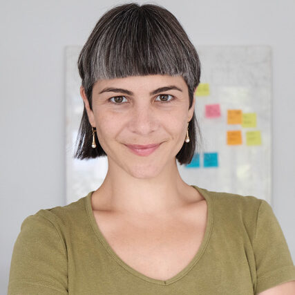 Bianca lächelt in die Kamera. Sie hat mittelange schwarze Haare mit grauen Strähnen und trägt ein olivgrünes T-Shirt.