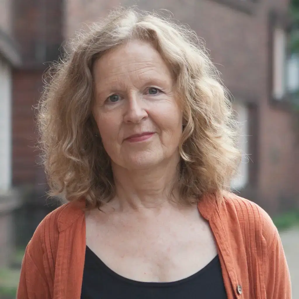 Anna lächelt in die Kamera. Sie hat schulterlange, blonde Haare und trägt ein orangefarbenes Hemd über einem schwarzen Top.