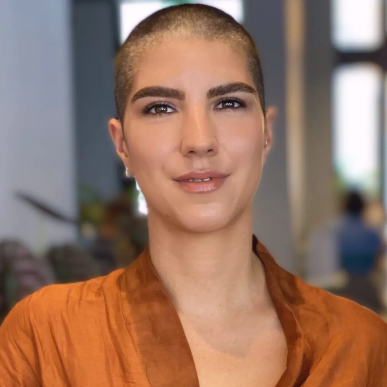 Malou schaut freundlich in die Kamera. Sie hat sehr kurze dunkle Haare und trägt eine orangefarbene Bluse.